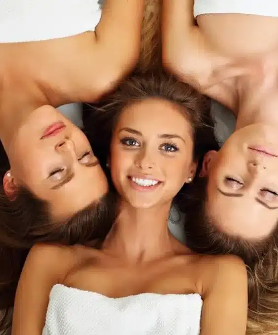 Drei junge Frauen liegen lächelnd nebeneinander und genießen eine Spa-Behandlung bei Behnaz's Beauty Bar
