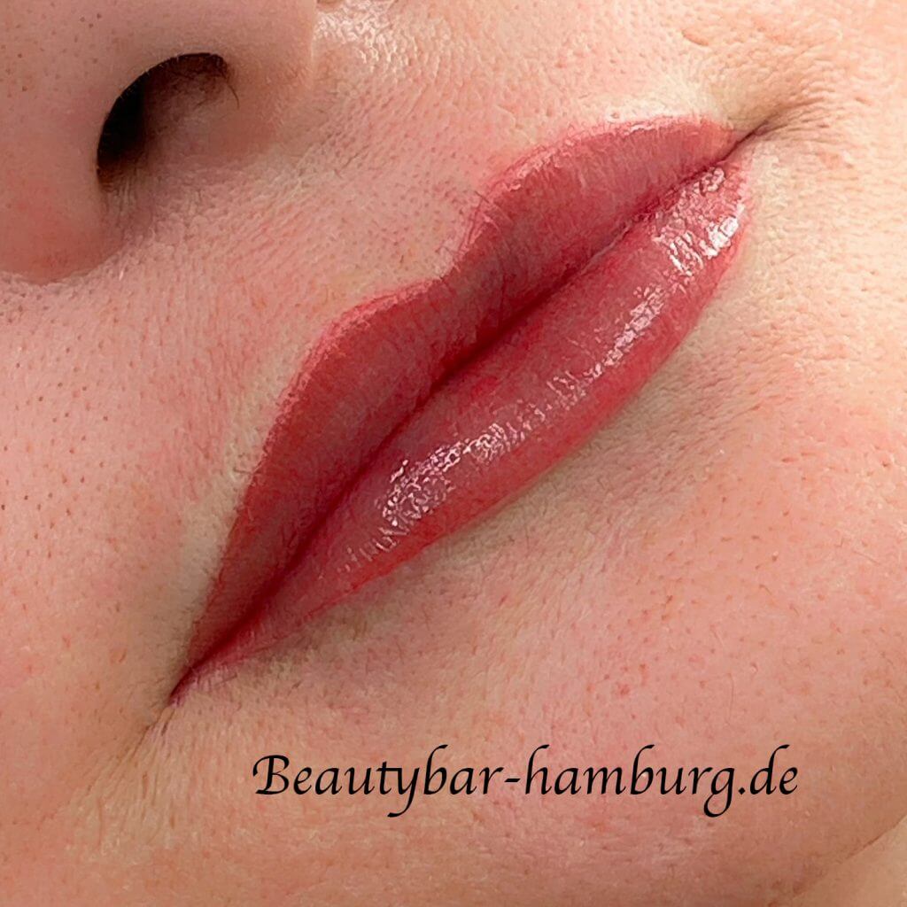 Makroaufnahme intensiv pigmentierter Lippen: Kräftig rot gefärbte, glänzende Lippen kurz nach einer Permanent-Make-up-Behandlung. Beautybar-hamburg.de Wasserzeichen sichtbar.