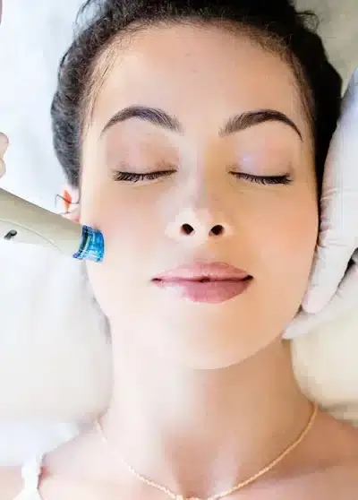 Frau mit geschlossenen Augen erhält eine Mikrodermabrasionsbehandlung im Gesicht bei Behnaz's Beauty Ba