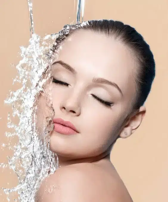 Frau mit geschlossenen Augen genießt einen erfrischenden Wasserstrahl auf ihrem Gesicht